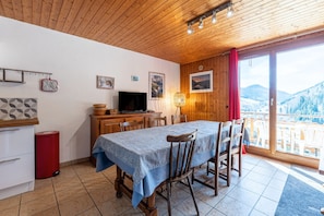 Un coin repas avec une table dressée pour quatre personnes, un téléviseur et une vue sur un paysage montagneux par le biais d’une grande fenêtre.