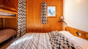 Une chambre dans un chalet en bois, avec des lits superposés, une fenêtre donnant sur un beau paysage et une lampe sur une table de chevet.
