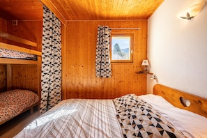 Une chambre dans un chalet en bois, avec des lits superposés, une fenêtre donnant sur un beau paysage et une lampe sur une table de chevet.