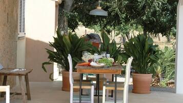 Un espacio de comedor al aire libre con una mesa lista para dos personas, rodeado de plantas en macetas y un colgante luminoso.