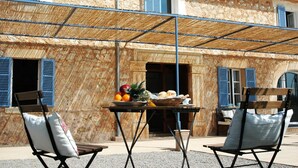 An outdoor seating area with a table set with fruits and bread, two folding chairs, and a building with stone walls and blue shutters. - Holiday Home 'Son Pelai Menut' with Mountain View, Wi-Fi and Air Conditioning (Illes Balears)