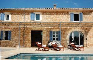 A stone building with a pool, outdoor seating, and a covered patio.