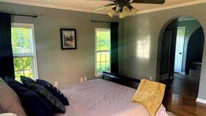 Un dormitorio con cama, ventilador de techo y dos ventanas.