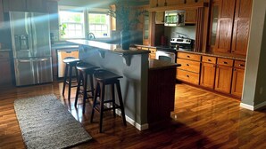 Una cocina con armarios de madera, un refrigerador de acero inoxidable, un microondas y una isla grande con taburetes.
