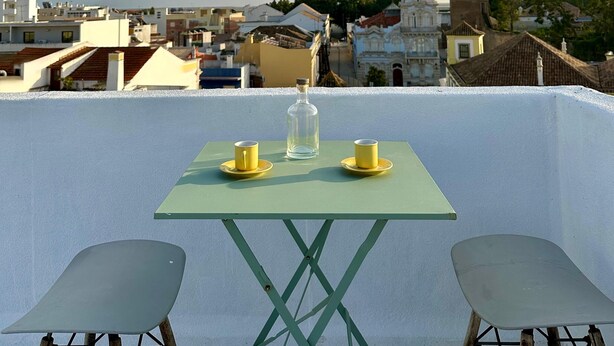 Una terrazza sul tetto con un tavolo e due sedie, affacciata su un panorama urbano con edifici storici.