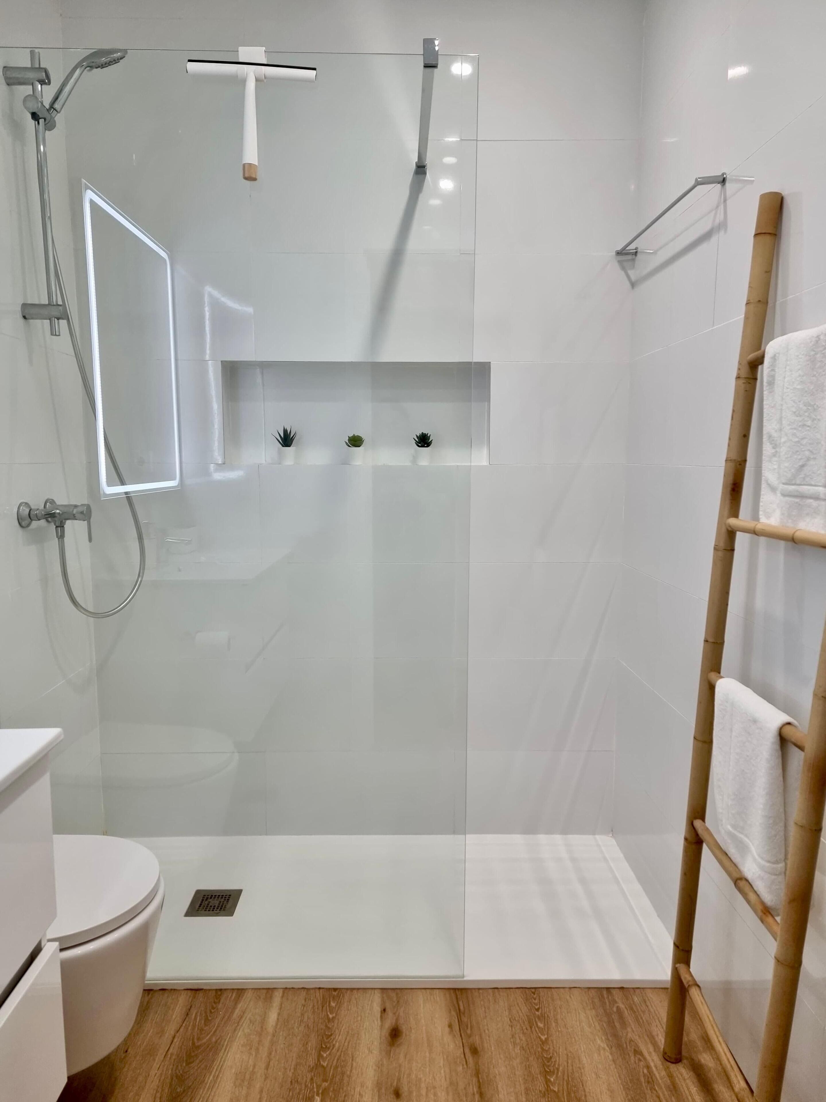 A modern bathroom with a glass-enclosed shower, a toilet, and a wooden floor.
