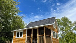 Una cabaña de madera con porche, varias ventanas y mobiliario exterior.
