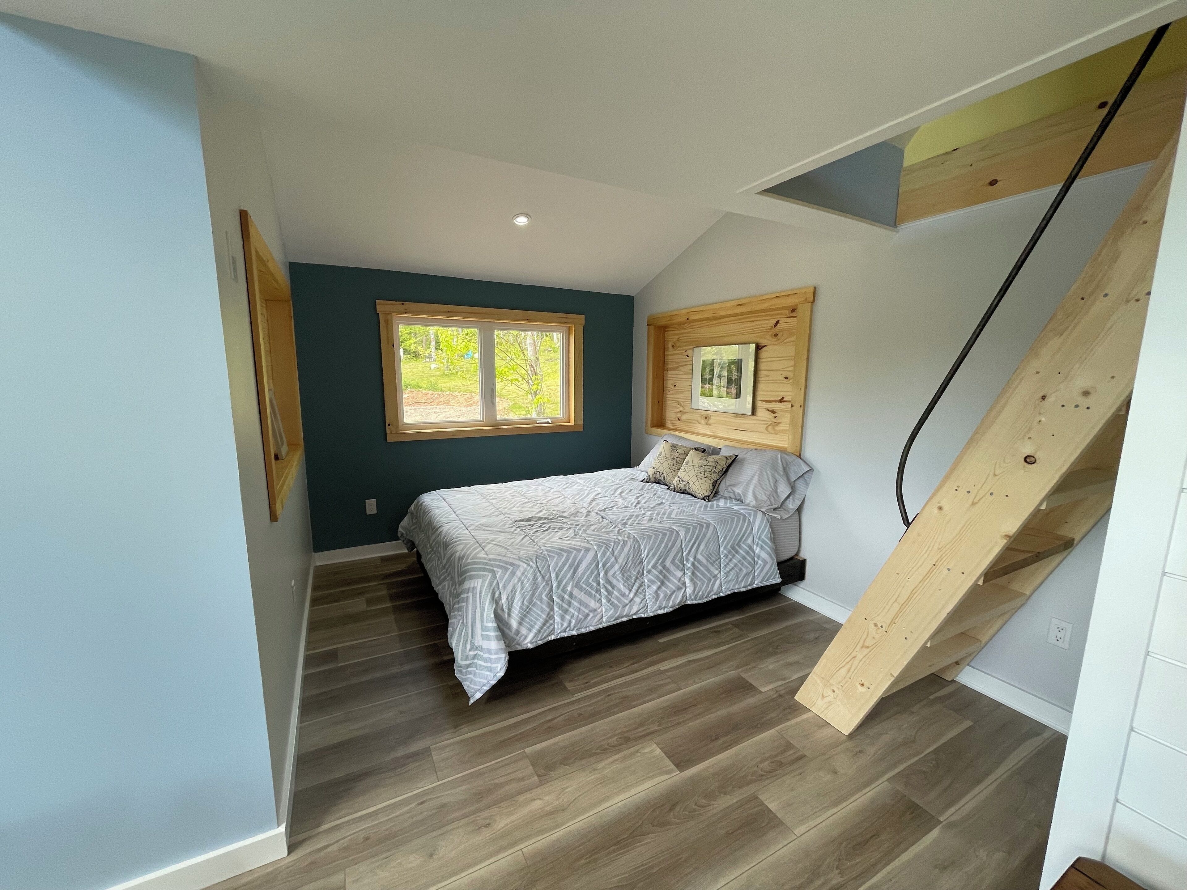 A bedroom with a bed, a window, a wooden headboard, and a staircase.