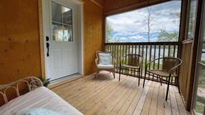 Una terraza de madera con una cama, dos sillas de mimbre y una puerta que da a una habitación.