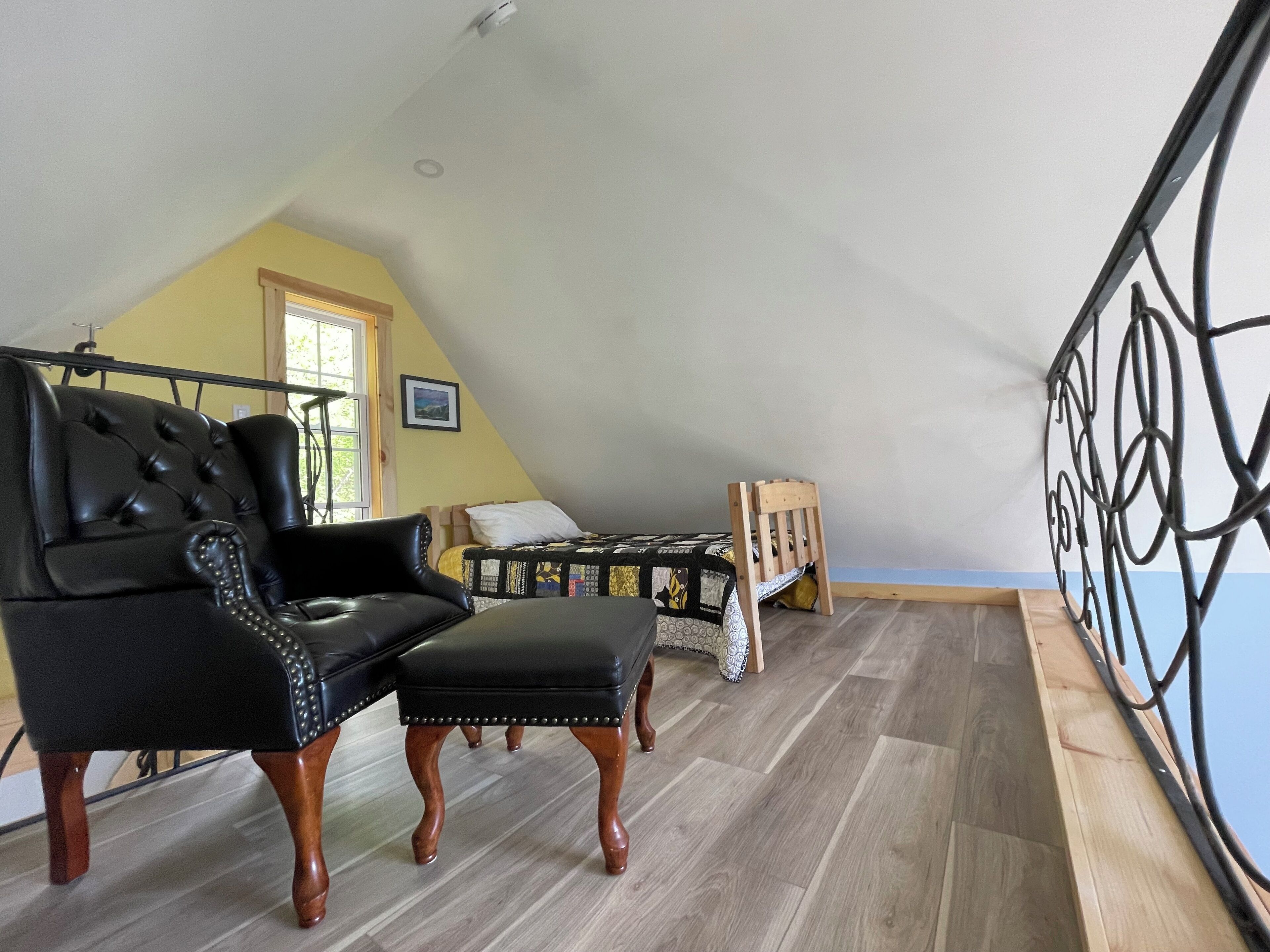 Una stanza con un divano in pelle nera, una sedia di legno, un letto con biancheria a motivi e un balcone.