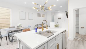 A modern kitchen with a central island, stainless steel appliances, and a unique chandelier. - Modern Heights Townhome 3BR with Fast Wifi & Free Park (Houston)