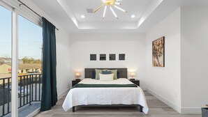 A modern bedroom with a large bed, a balcony with curtains, a ceiling light, and artwork on the wall. - Modern Heights Townhome 3BR with Fast Wifi & Free Park (Houston)