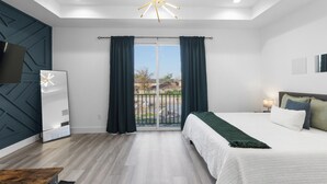 A modern bedroom with a large bed, a TV, and a balcony with curtains. - Modern Heights Townhome 3BR with Fast Wifi & Free Park (Houston)