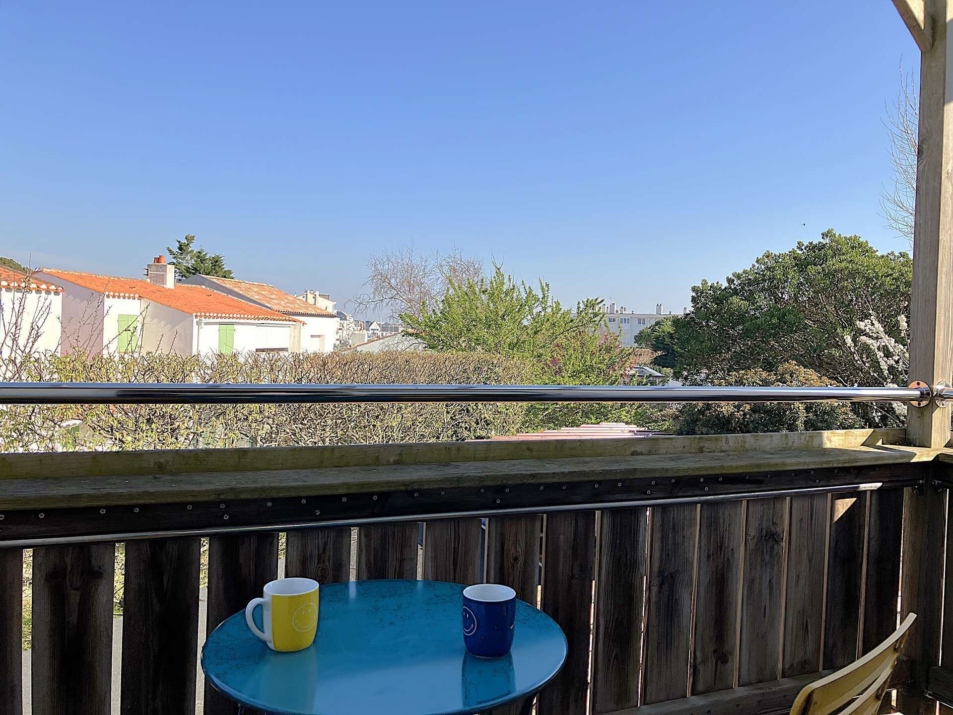 A balcony with a wooden railing, a small round table, and two mugs.