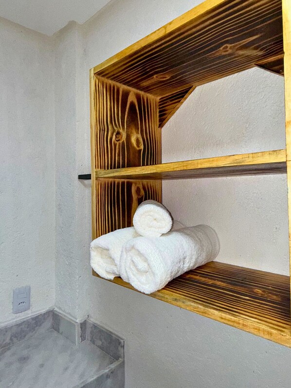 Une salle de bain avec une étagère en bois sur laquelle sont pliés des serviettes.