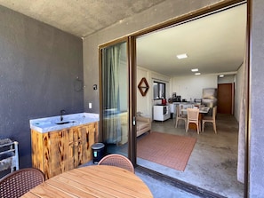 Un espacio habitable compacto con kitchenette, comedor y puerta corrediza de vidrio que da a un balcón.