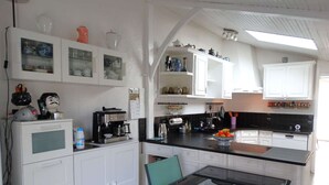 A compact kitchen with white cabinetry, a coffee machine, and a glass dining table. - Les Treilles Saint Hilaire de Riez (SAINT HILAIRE DE RIEZ)