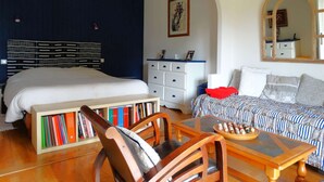 A bedroom with a bed, a dresser, a sofa, a chair, a table with a board game, a bookshelf, and a mirror. - Les Treilles Saint Hilaire de Riez (SAINT HILAIRE DE RIEZ)