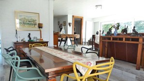 A dining area with a long wooden table, colorful chairs, and a view of the outdoors. - Les Treilles Saint Hilaire de Riez (SAINT HILAIRE DE RIEZ)