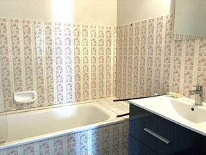 Um banheiro com azulejos estampados com flores, uma banheira branca, uma pia com espelho e um armário.