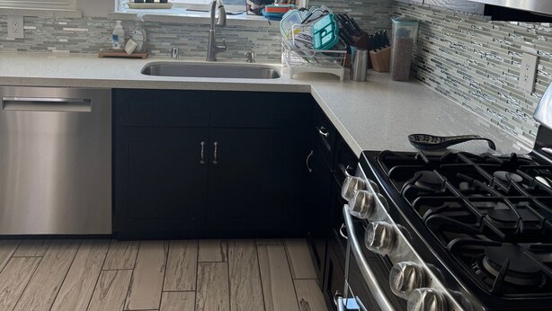 A modern kitchen with a stainless steel sink, black cabinets, a stove, and a window with potted plants.