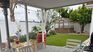 A covered outdoor dining area with a table and chairs, a water feature, and a view of the backyard.