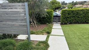 A paved pathway leading to a gate, surrounded by well-maintained grass and bushes.