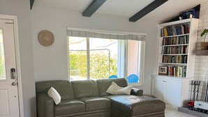 A living room with a sectional sofa, a patterned rug, a bookshelf, and a window with a view of greenery.