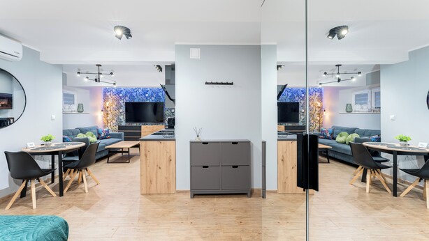 A modern living room with a sofa, coffee table, and TV. There is a kitchen area with a dining table and chairs.