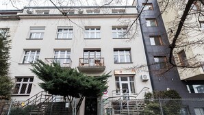 A multi-story building with a central entrance, a small balcony with outdoor furniture, and a sign indicating a business or service on the ground floor. - Underground Mystique Apartment (Kraków)