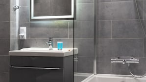 A modern bathroom with a glass shower enclosure, a white sink with a mirror above it, and a toilet. - Underground Mystique Apartment (Kraków)