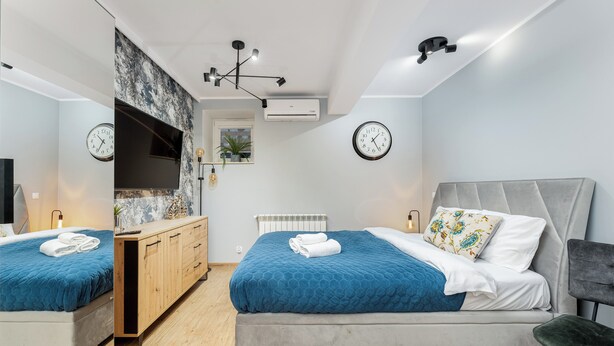 A modern bedroom with two beds, a TV, and a wooden cabinet. - Underground Mystique Apartment (Kraków)