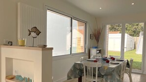 Un coin repas avec une table dressée pour quatre personnes, un décor mural représentant un poisson et une vue sur le jardin à travers la porte.