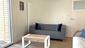 Un salon avec un canapé gris, une table basse en bois et une porte dotée d’un panneau en verre dépoli.