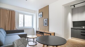 A modern living room with a grey sofa, a round black table, and a small round table. There is a wooden cabinet with a TV and a kettle on top.