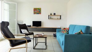 Una sala de estar moderna con un sillón negro, un sofá azul, una mesa de centro, un televisor y un cuadro colorido en la pared.