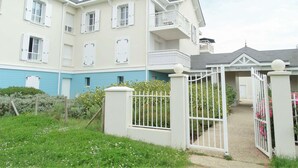 Un edificio residencial de varios pisos con entrada protegida, un piso inferior azul y pisos superiores blancos.