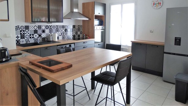 Una cocina moderna con una mesa de madera, sillas negras, horno empotrado y refrigerador de acero inoxidable.