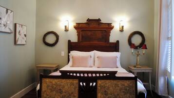 A bedroom with a wooden headboard, two wall sconces, a bedside table with a lamp, and two framed floral artworks on the wall.