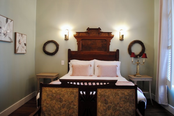 Un dormitorio con cabecera de madera, dos apliques, una mesita de noche con lámpara, y dos obras de arte floral enmarcadas en la pared.