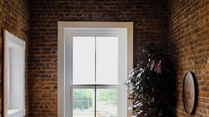 Ein gemütliches Zimmer mit Backsteinwand, großem Fenster, Holzwand und einem Blumentopf.