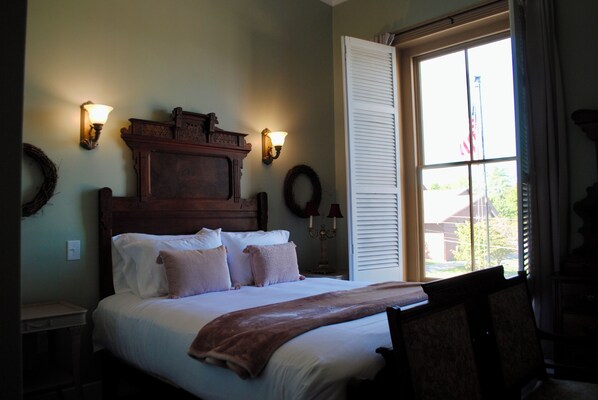 A neatly made bed with a headboard, two wall sconces, and a window with blinds. - The Lodge at Old City Hall (Jefferson City)