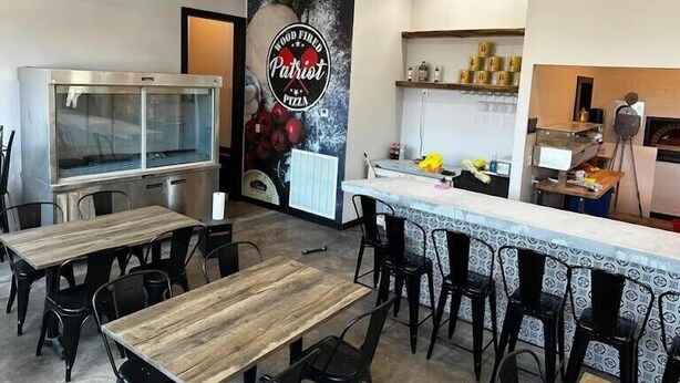 Ein Restaurantinneres mit Holzbalkendecke, einem Pizzaofen, einer Theke mit Barhocker und einem großen Pizza-Schild an der Wand.