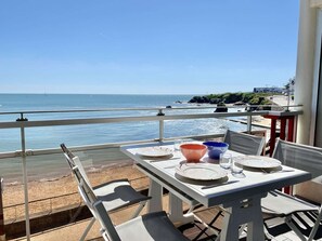 Ein Balkentisch mit Tellern, Schüsseln und Gläsern, mit Blick auf Strand und Meer.