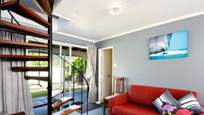 A modern living room with a red sofa, a staircase, and a painting of a seascape. - Okiwi Bay Bach with Bay Views (Ōkiwi Bay)