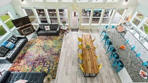 A spacious living area with a large wooden dining table, multiple chairs, a sofa, and a TV.