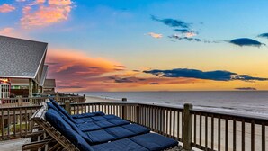 A wooden deck with lounge chairs and a building with a sloped roof overlooking the beach.