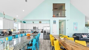 A modern kitchen with white cabinets, a central island with blue chairs, and a dining area with yellow chairs.