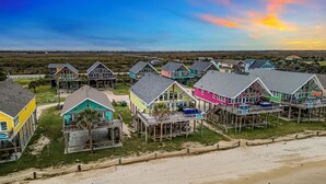 A coastal area with colorful beach houses on stilts, a sandy beach, and a clear sky.