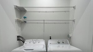 A laundry room with two white front-loading washing machines and a metal shelf above them. - Welcome to outlet Charming townhome with WiFi and AC & more in enjoyable Bayonne (Bayonne)
